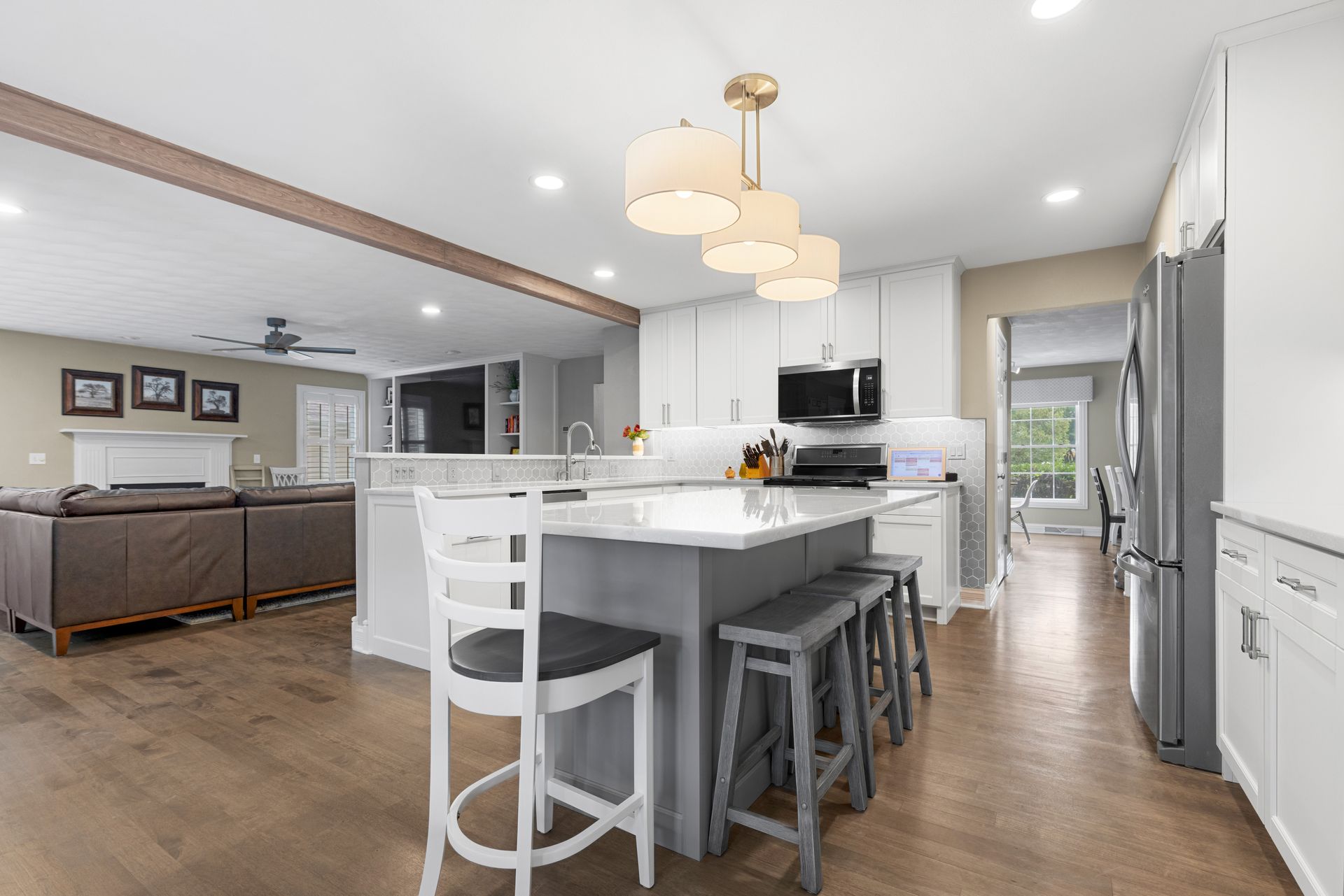 Modern kitchen with island, stools, and open view to living room with hardwood floors and white cabinetry.