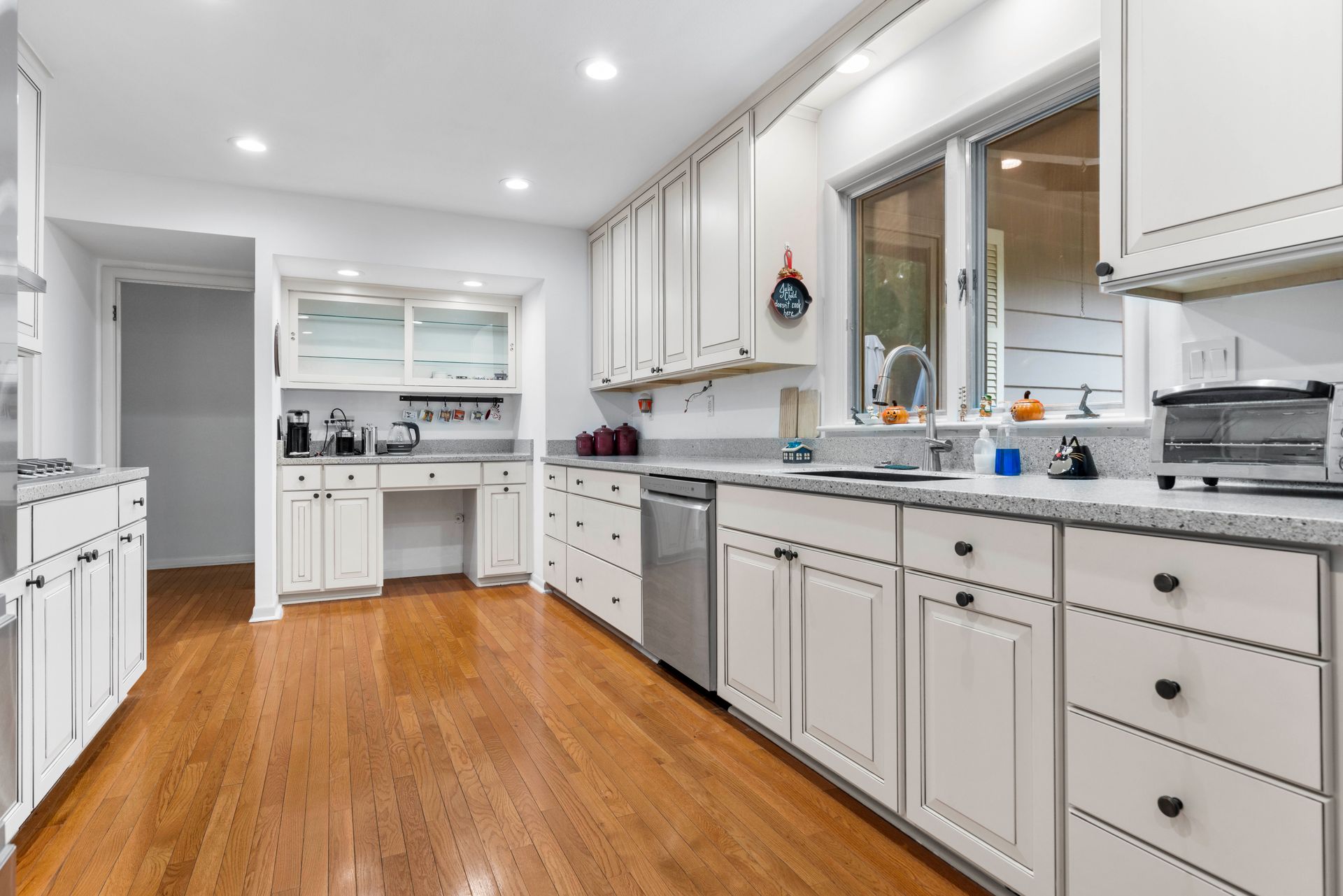 Bright kitchen with white cabinets, granite countertops, stainless steel appliances, and hardwood floors.