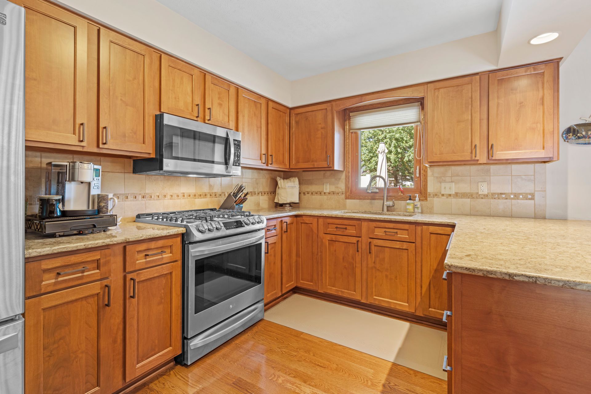Wooden kitchen cabinets with stainless steel appliances, granite countertops, and a window.