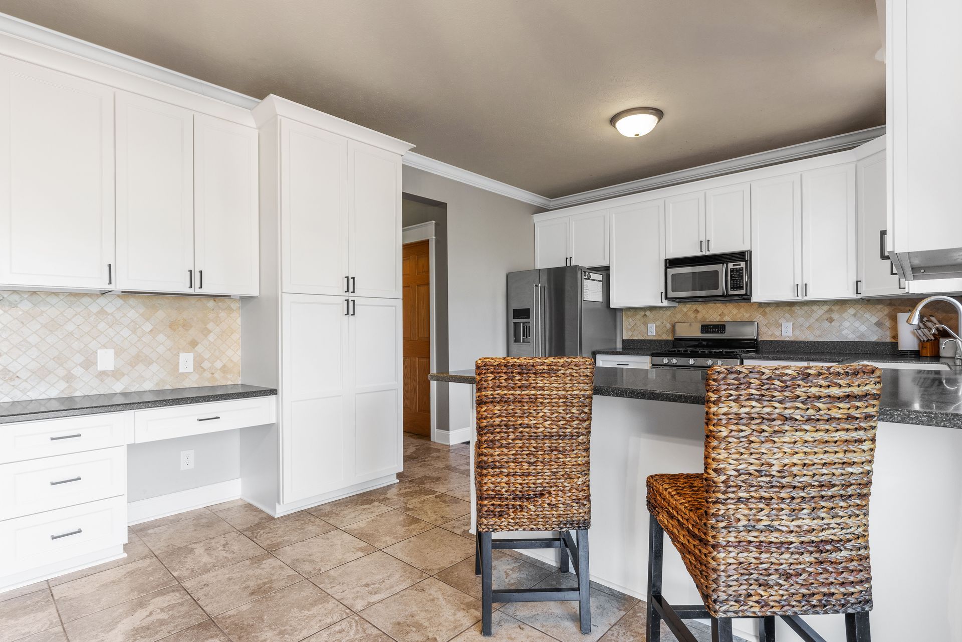 White kitchen with cabinets, countertops, and two woven bar stools.