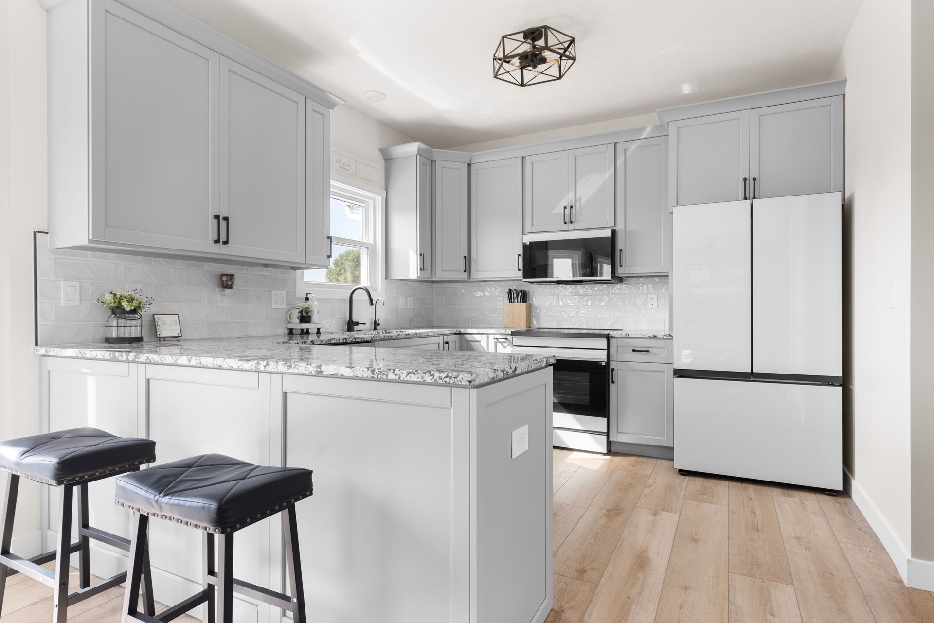 A modern kitchen with gray cabinets, white countertops, stainless steel appliances, and an island with bar stools.