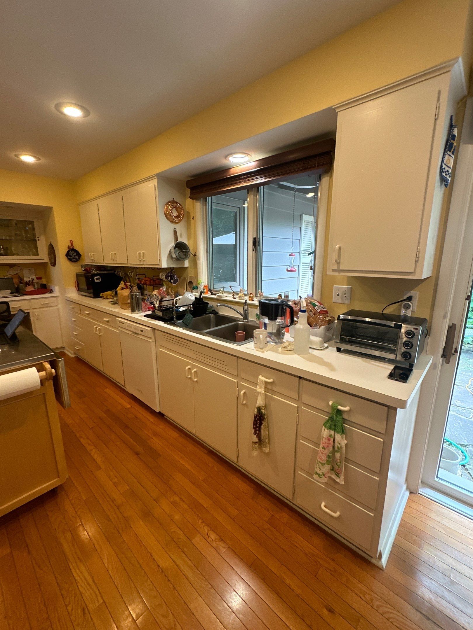 Kitchen with white cabinets, wood floor, and a window overlooking a yard.