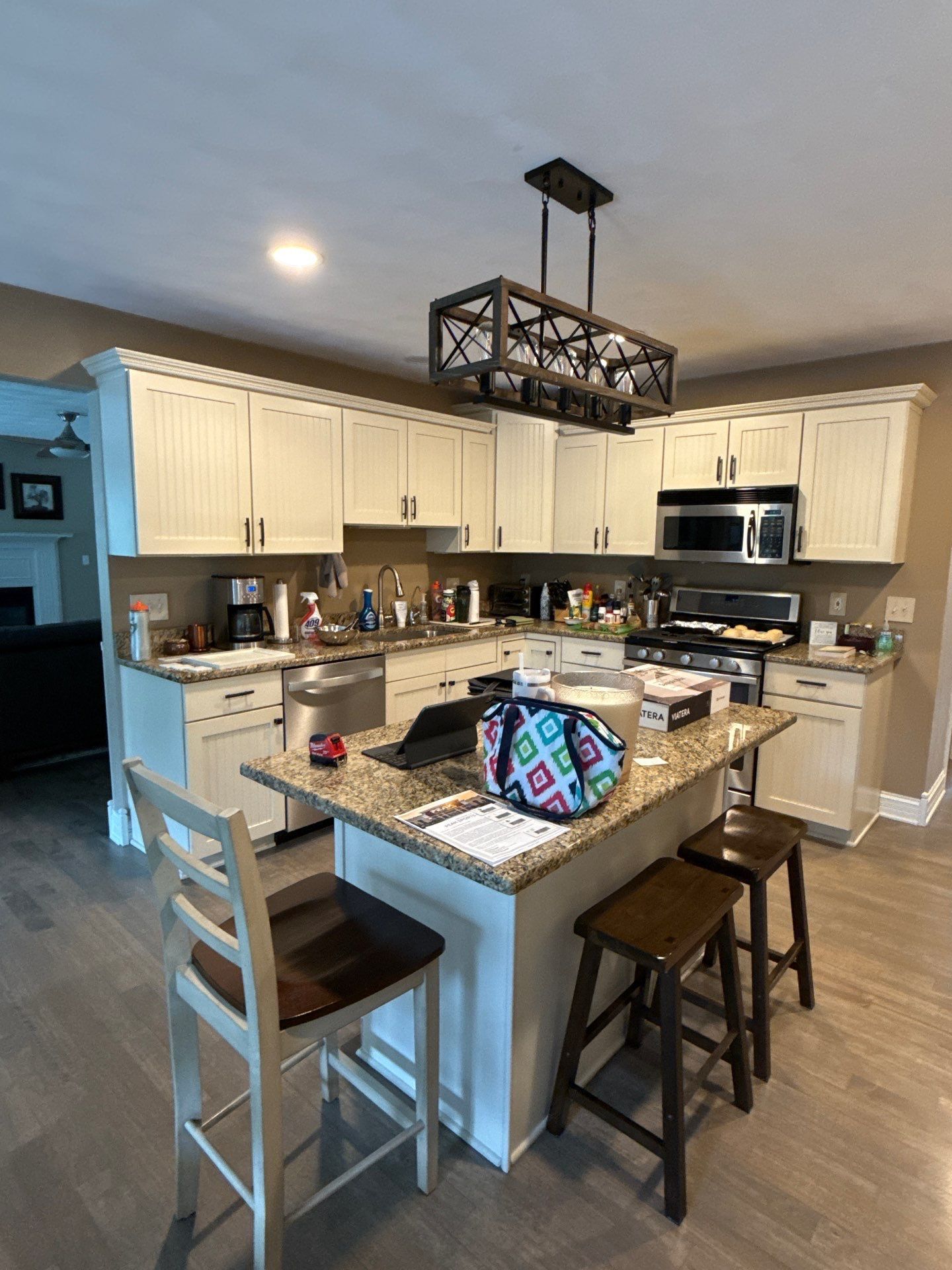 Kitchen with white cabinets, island, and wood floors. A light fixture hangs overhead, and there are bar stools.