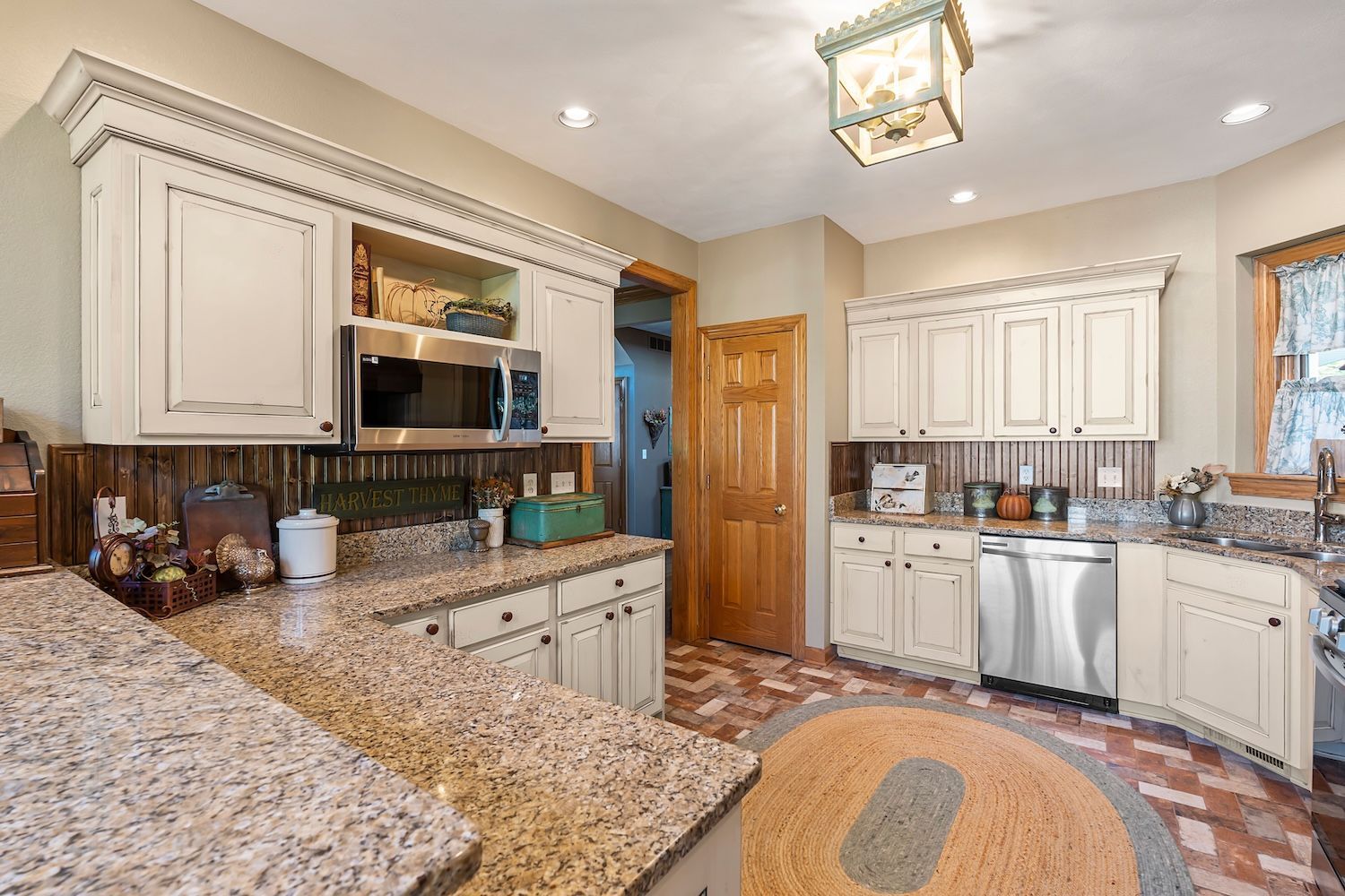 Cream-colored kitchen with granite countertops, light cabinets, stainless steel appliances, and a round rug.
