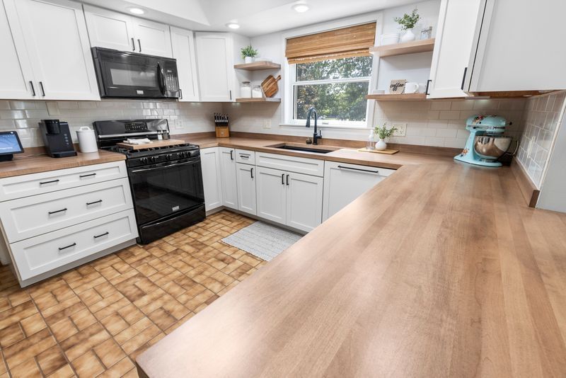 White kitchen with light wood countertops, white cabinets, black appliances, and wood flooring.