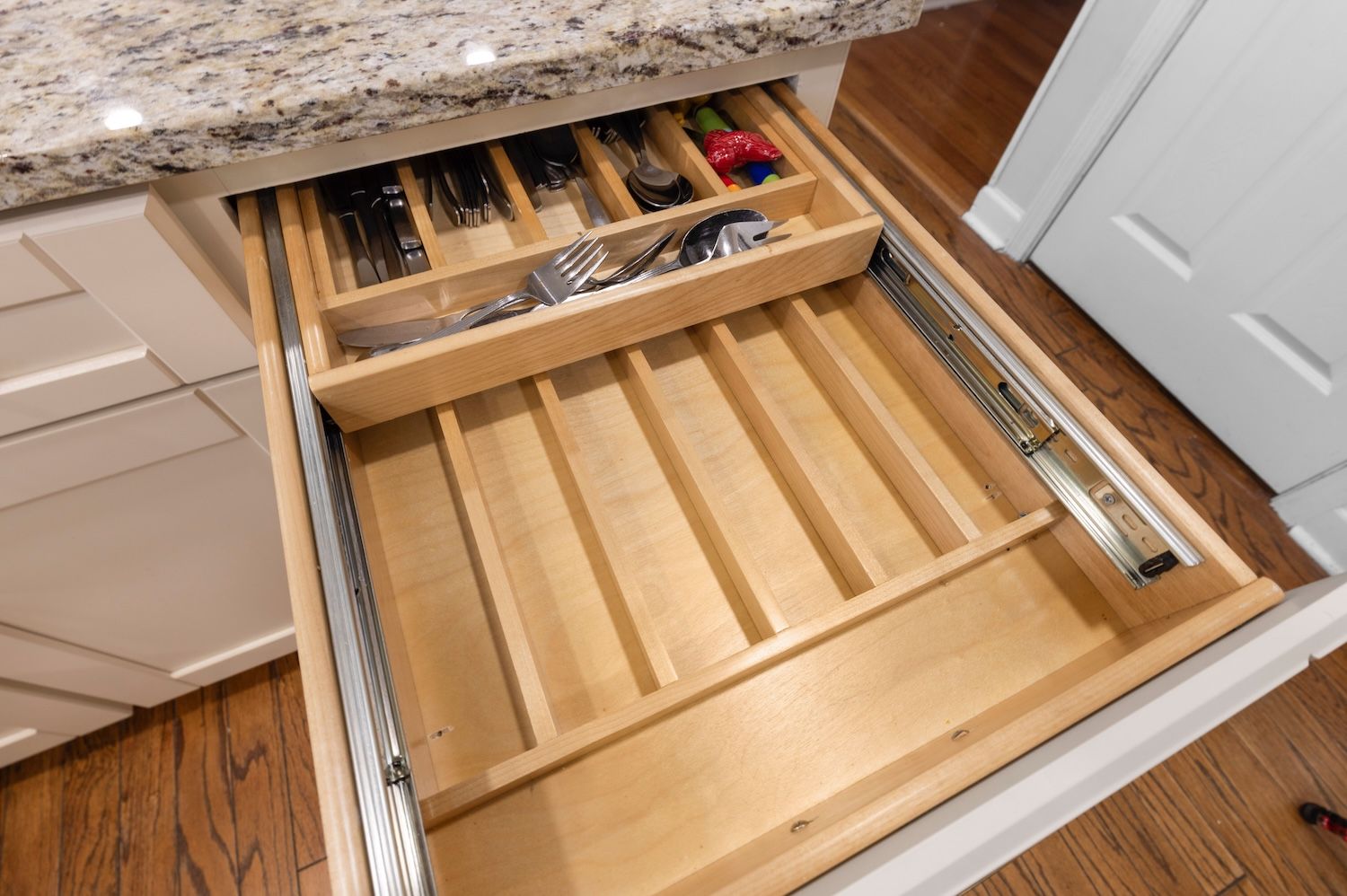 Open kitchen drawer with silverware organizer, showcasing wood grain and marble countertop.