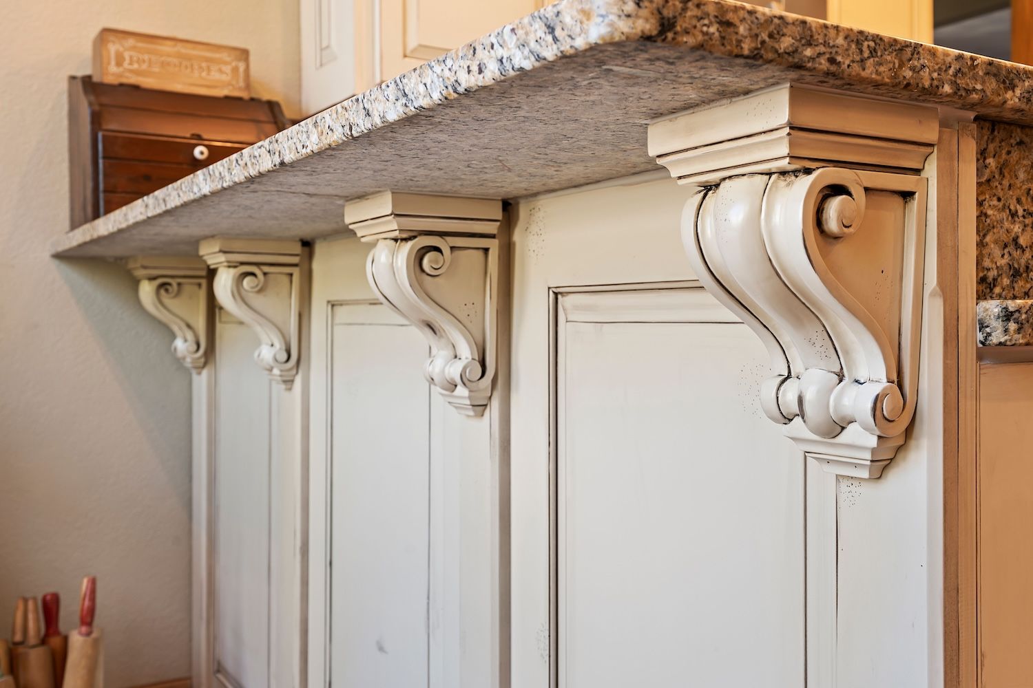 Cream-colored kitchen island with granite countertop, supported by ornate corbels.