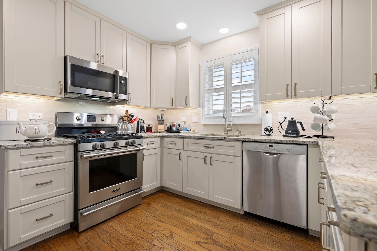 Modern kitchen with white cabinets, stainless steel appliances, and wooden floors.