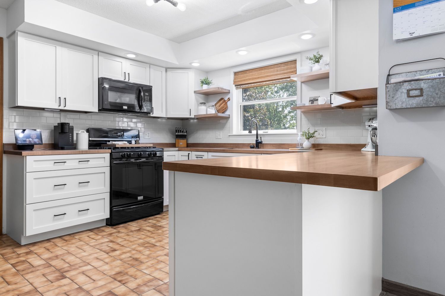 White kitchen with black appliances, butcher block countertops, and wooden flooring.