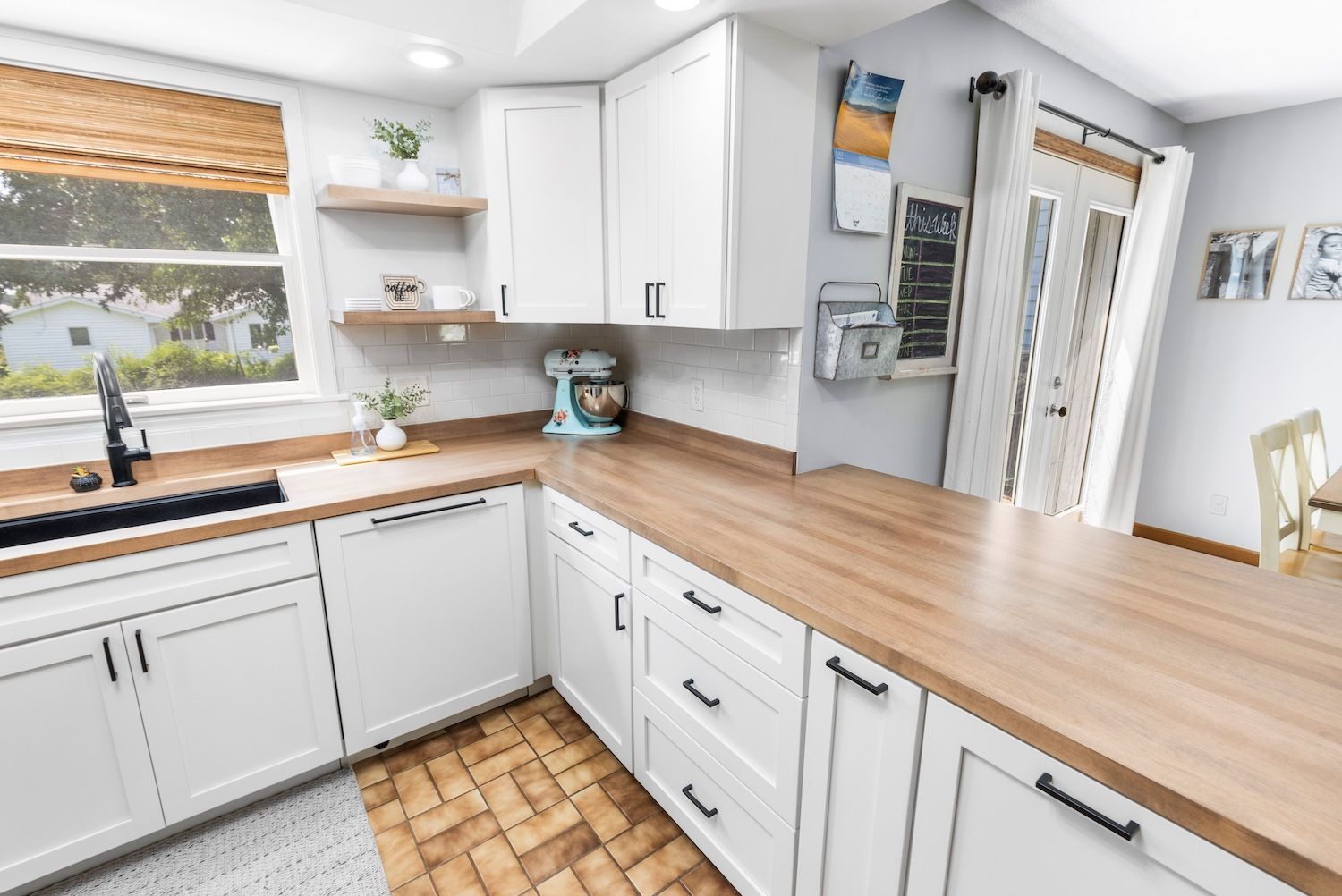 White kitchen with wooden countertops and cabinets, black hardware, and a teal mixer.