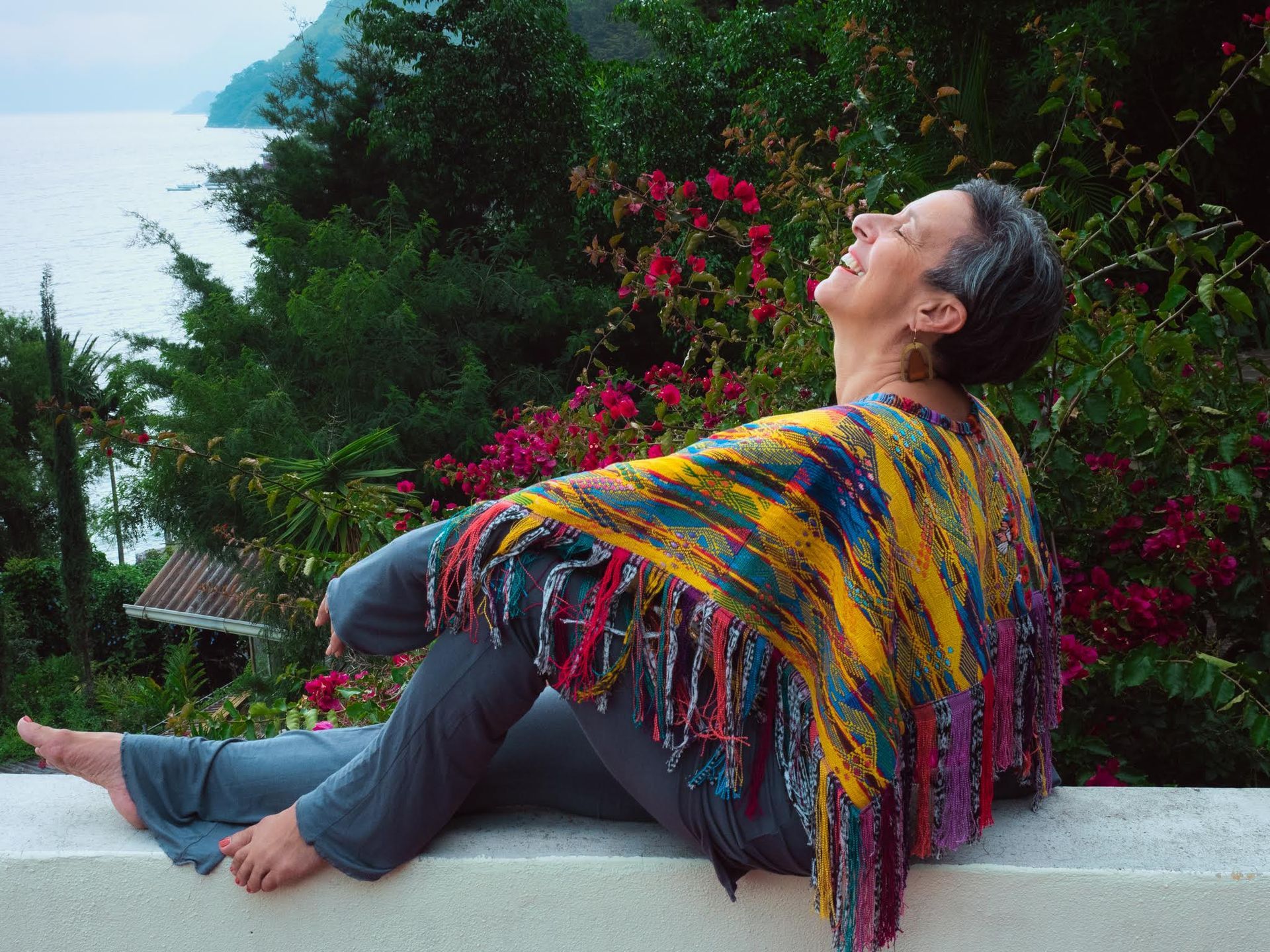 A woman wearing a colorful shawl is sitting on a wall