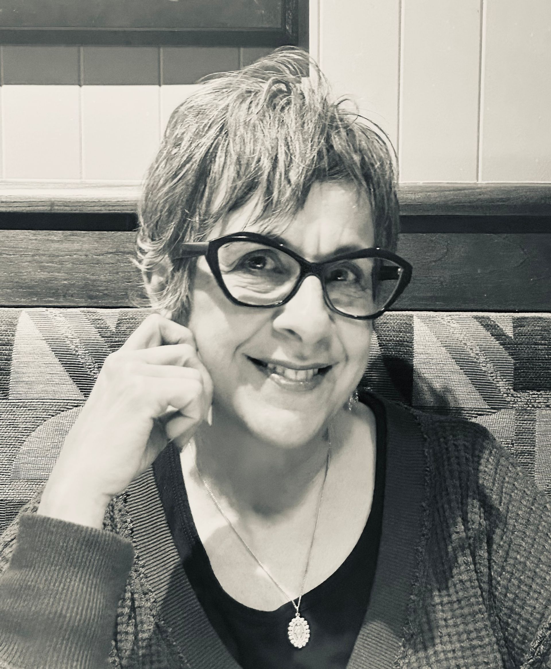 A woman wearing glasses and a necklace is smiling in a black and white photo.