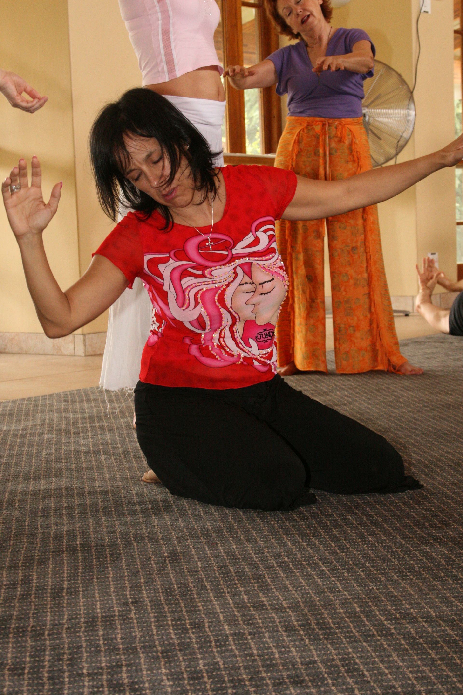 A woman in a red shirt is kneeling on the floor with her arms outstretched
