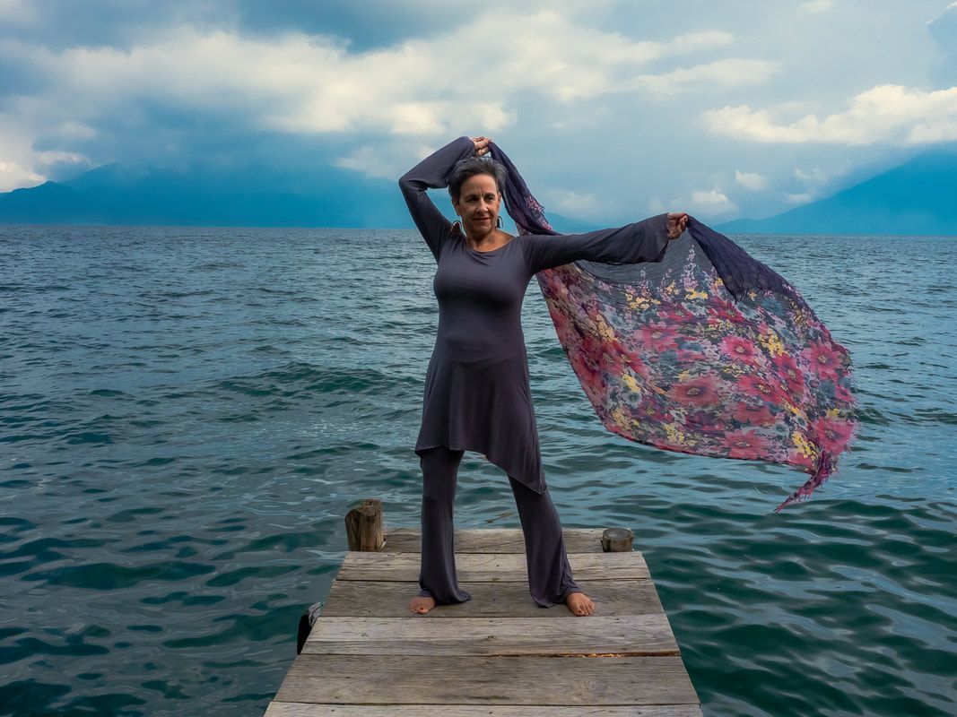 A woman is standing on a dock holding a scarf over her head.