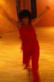 A woman in a red dress is dancing on a wooden floor.