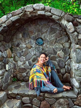A woman is sitting on the ground in front of a stone wall.