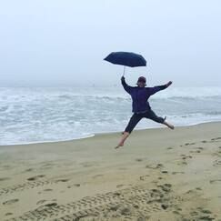 A person is jumping in the air while holding an umbrella on a beach.