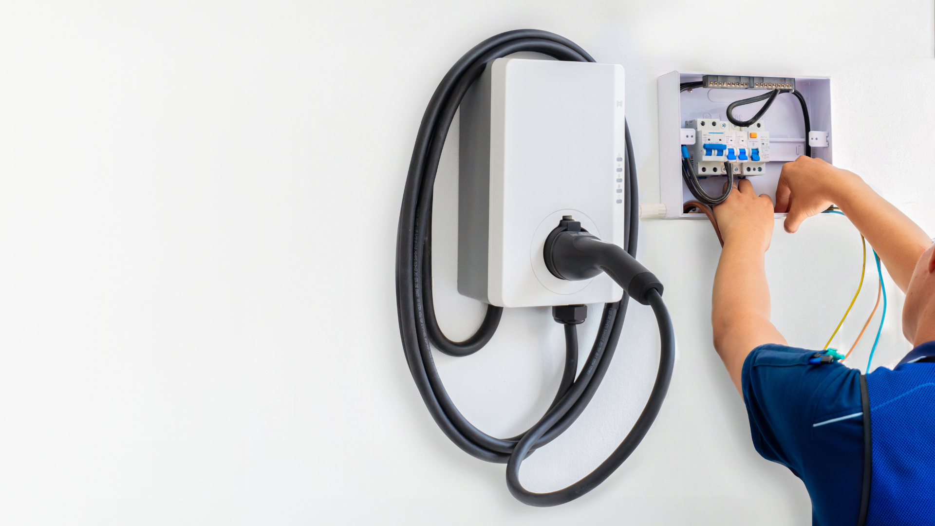 An electrician near open electrical box connected to EV charger on white wall; potentially unsafe activity.
