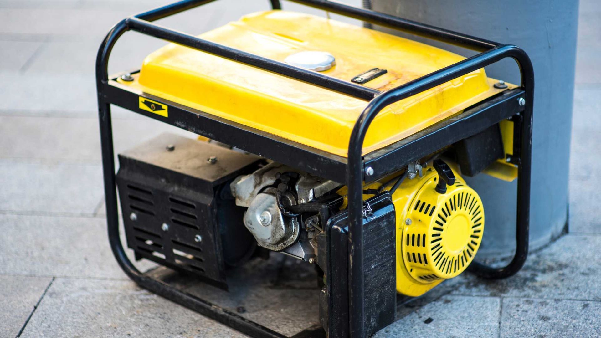 A yellow generator is sitting on the sidewalk next to a trash can.