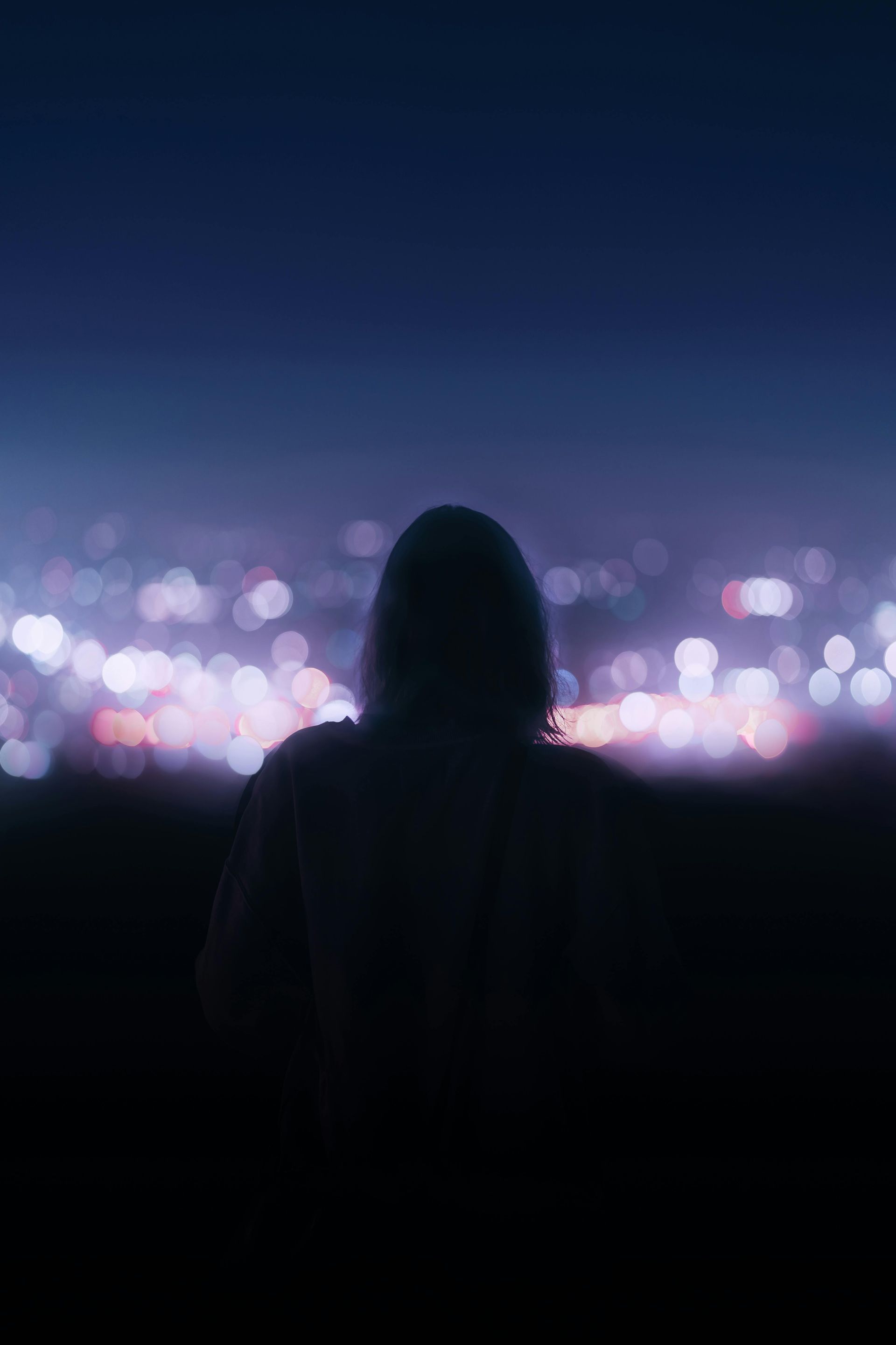 Silhouette of a person looking out at a blurred city skyline at night, with purple and white lights.