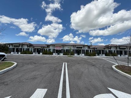 Hilera de casas adosadas modernas con aparcamiento y un cielo azul con nubes.