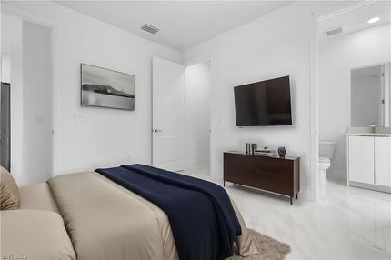 Dormitorio con cama, televisor, cómoda y un pequeño baño. Paredes blancas en su mayoría, con detalles en azul y marrón.