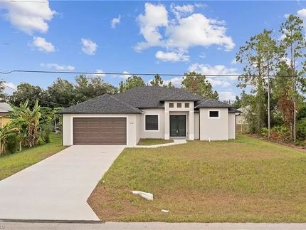 Una casa de una sola planta, de color claro, con una puerta de garaje marrón y un techo gris sobre un césped bajo un cielo azul.
