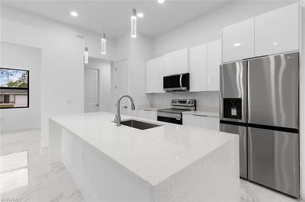 Cocina moderna con gabinetes blancos, electrodomésticos de acero inoxidable y una isla central.