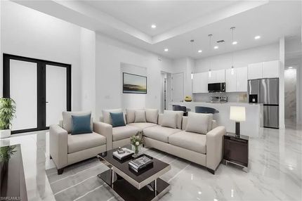 Sala de estar moderna con paredes blancas, sofá seccional, mesa de café y cocina abierta.