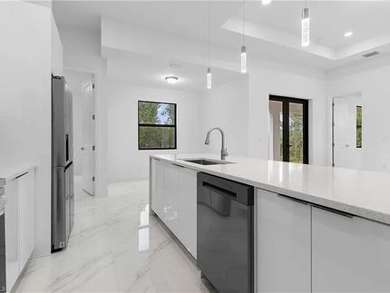 Cocina blanca moderna con isla, electrodomésticos de acero inoxidable y pisos de mármol.