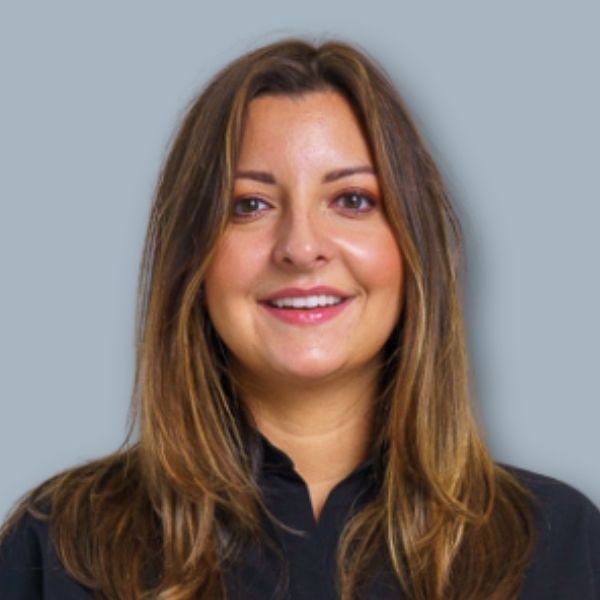 A woman wearing a plaid jacket and earrings is smiling for the camera.