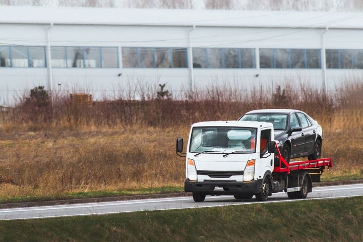 Tow truck carrying a black car on a road next to a building.