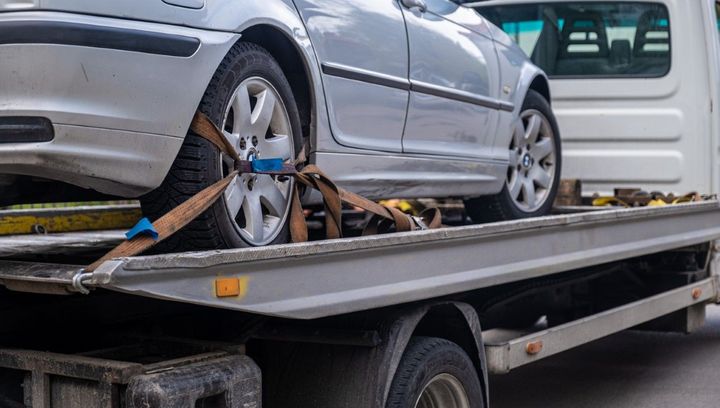 Silver car being towed on a flatbed tow truck, secured with straps.