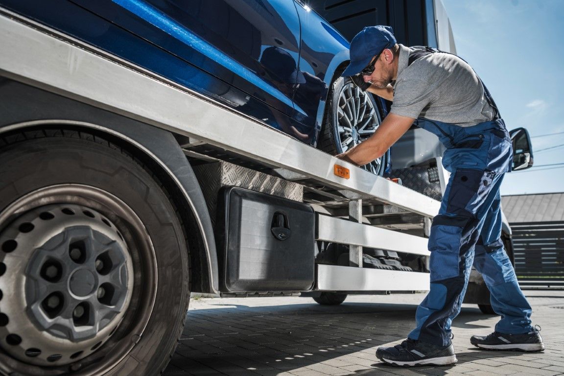 A tow truck operator secures a blue car onto the flatbed.