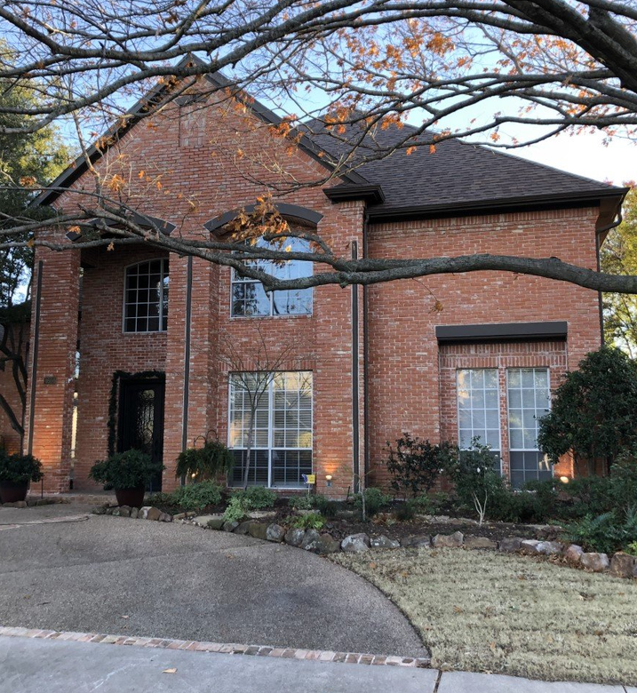 A large brick house with a driveway and trees in front of it