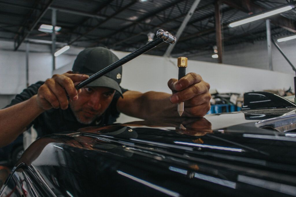 Man using tools to repair car dent in a workshop.