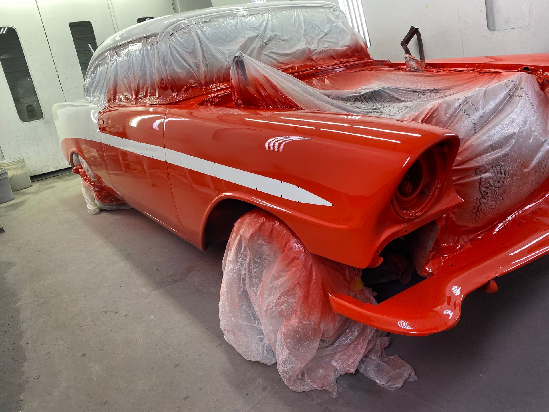 Classic car, red and white paint, being restored in a garage.