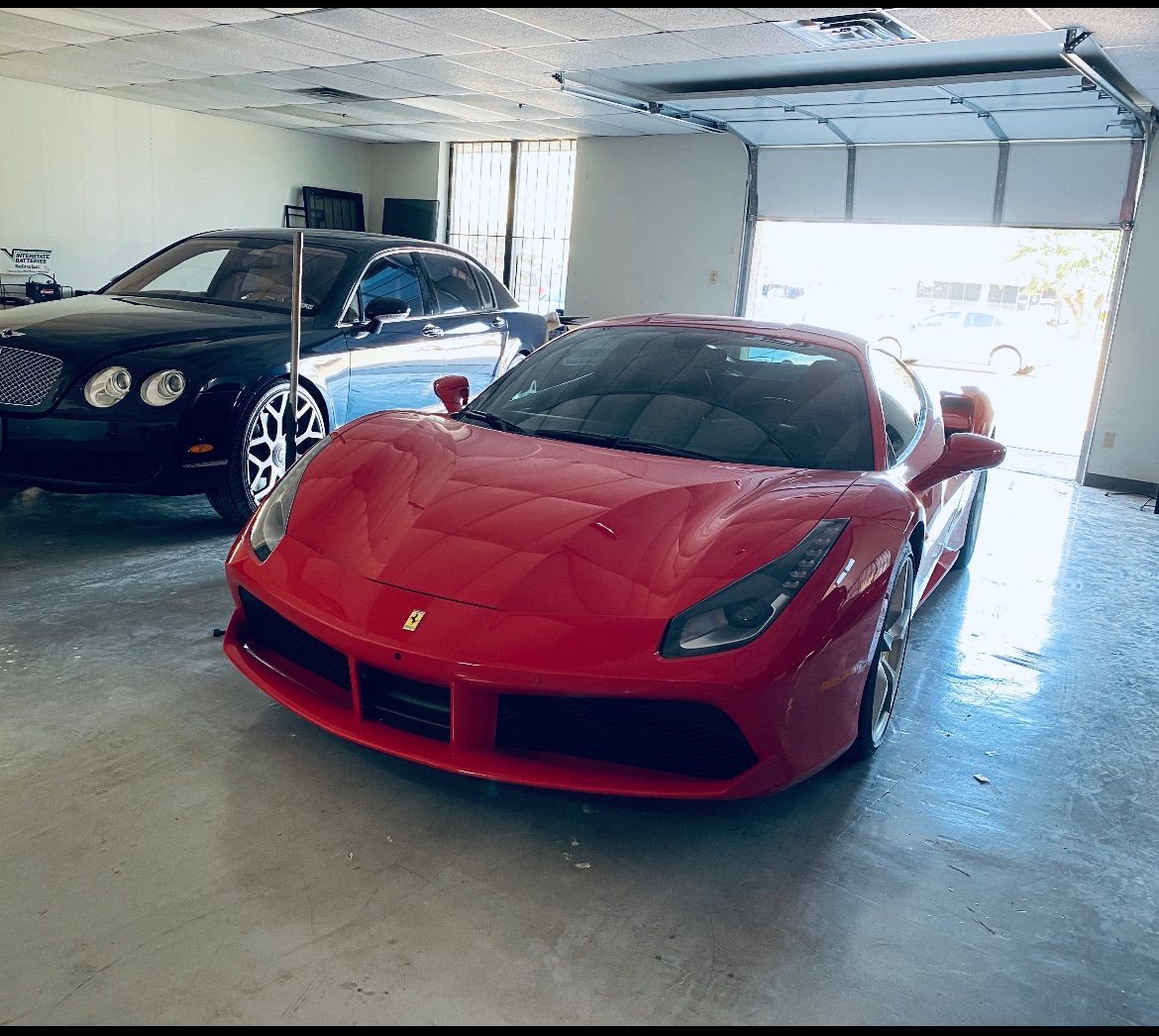 Red Ferrari and black Bentley parked in a garage with the garage door open.