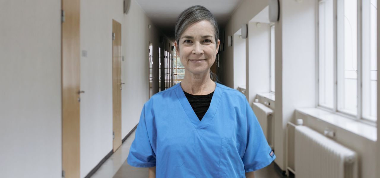 A woman in a blue scrub is standing in a hospital hallway.