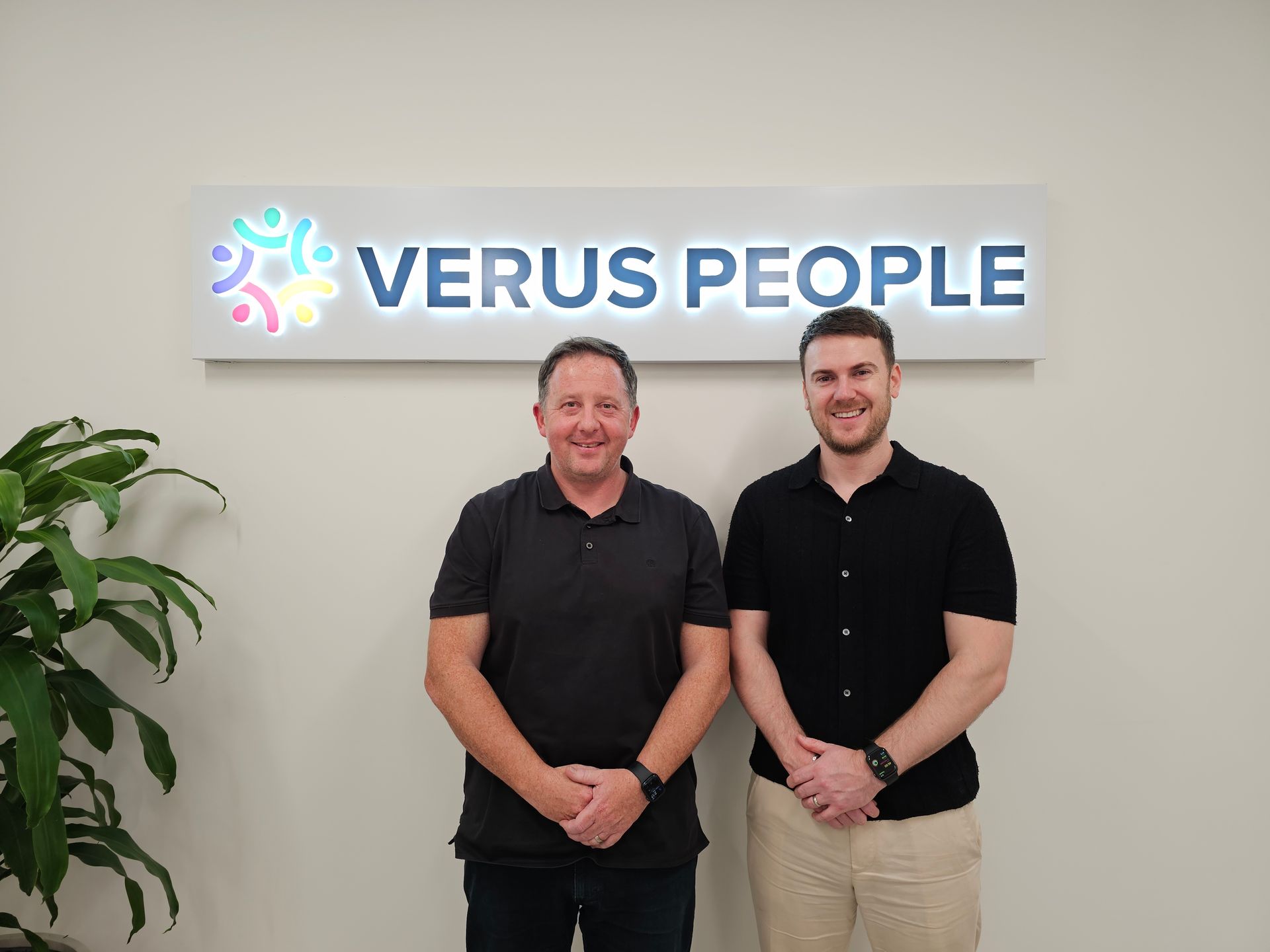 Two men standing in front of a sign that says verus people