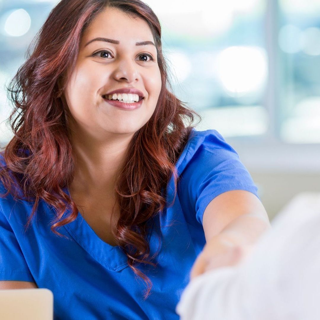 A woman in a blue scrub top is smiling while talking to a patient.