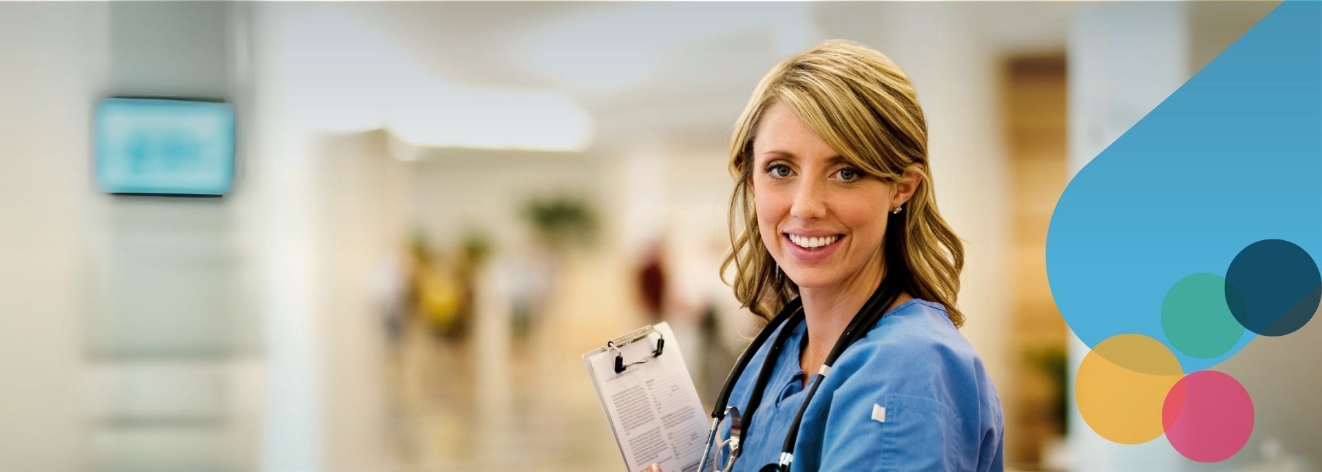 A nurse with a stethoscope around her neck is smiling while standing in front of a building.