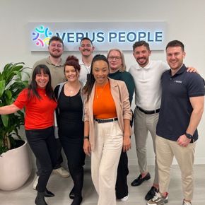 A group of people posing for a picture in front of a verus people sign