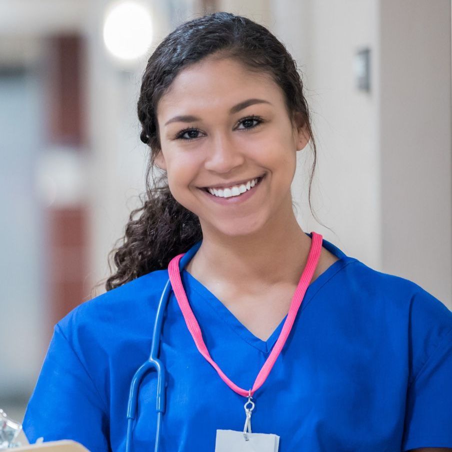 A nurse with a stethoscope around her neck is smiling and holding a book.