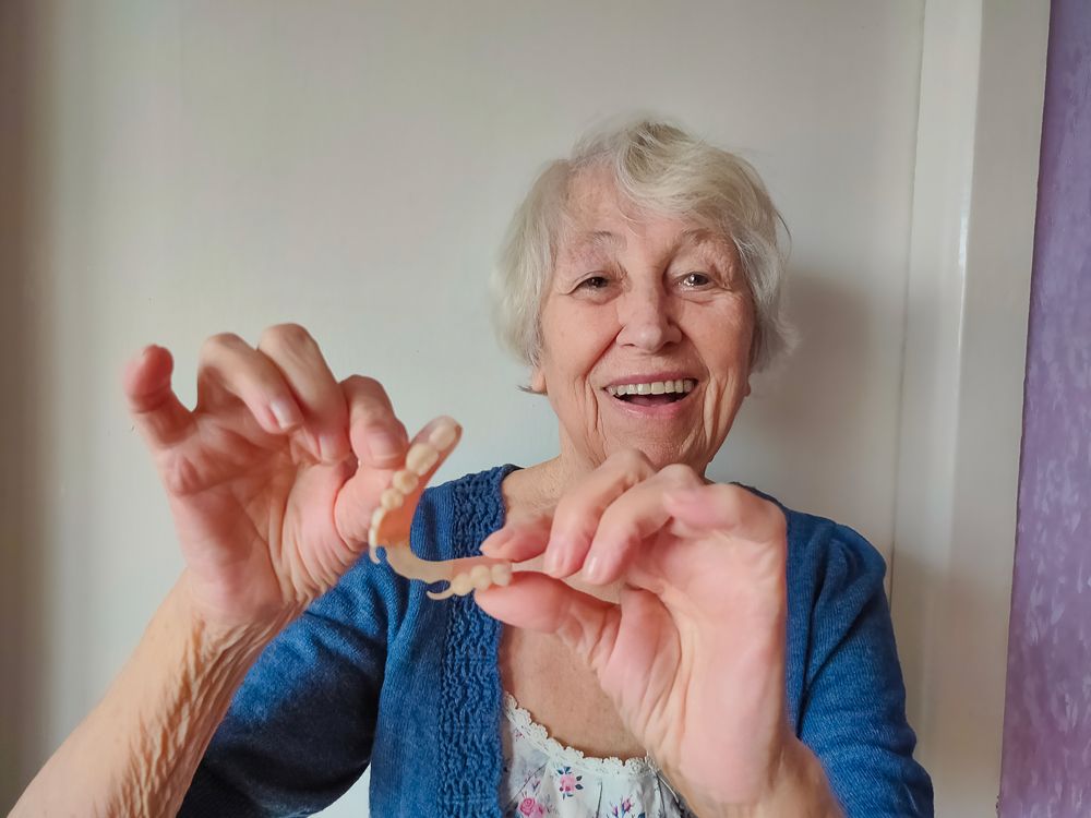 Old Woman Holding Her Dentures — Central Coast, NSW — Peninsula Denture Centre