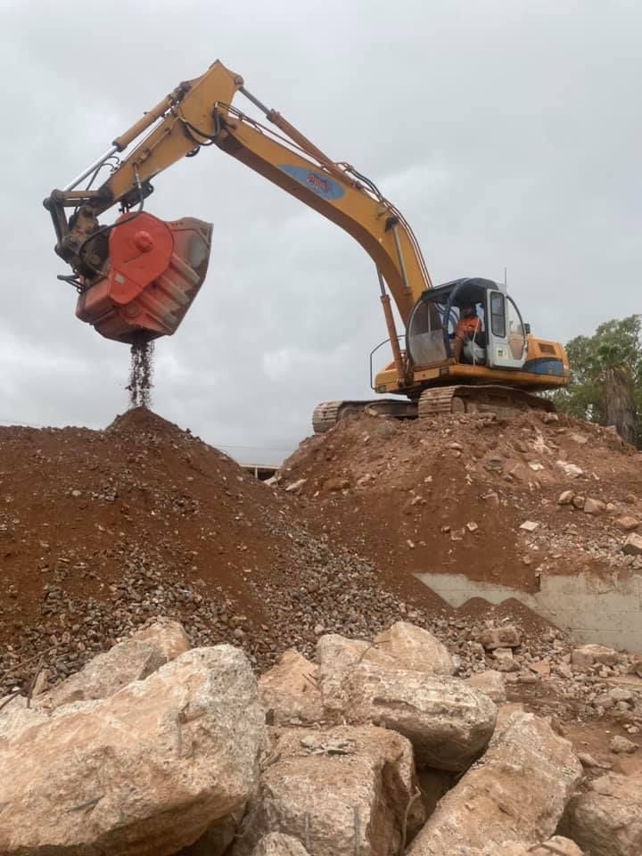 A yellow excavator is working on a pile of rocks — Bullant Building In Ciccone, NT