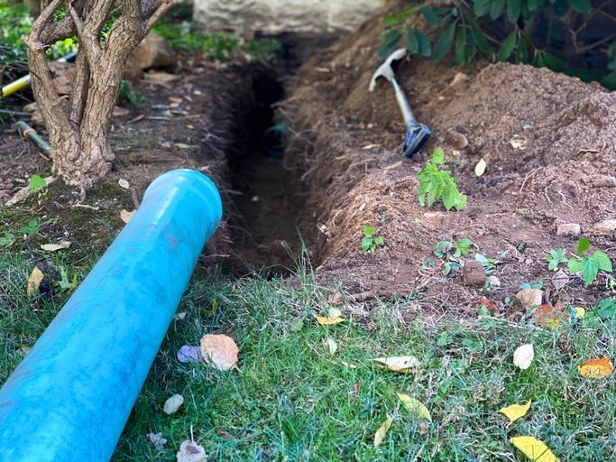 A blue pipe is sitting in the grass next to a hole in the ground.