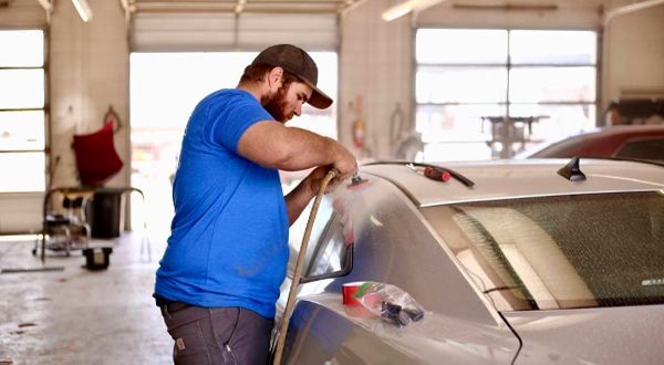 A man in a blue shirt is working on a car in a garage.