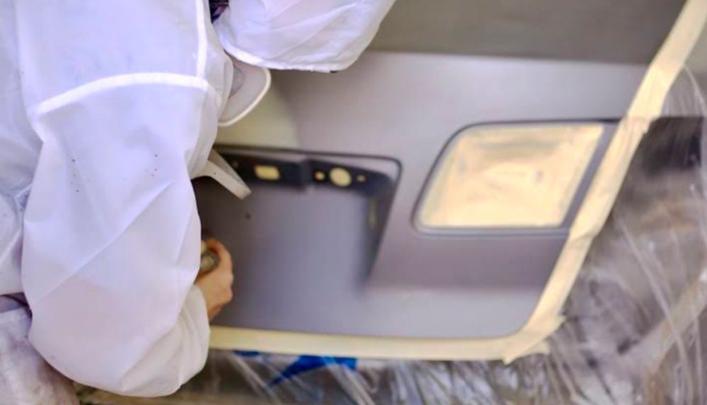 A person in a protective suit is working on a car door.
