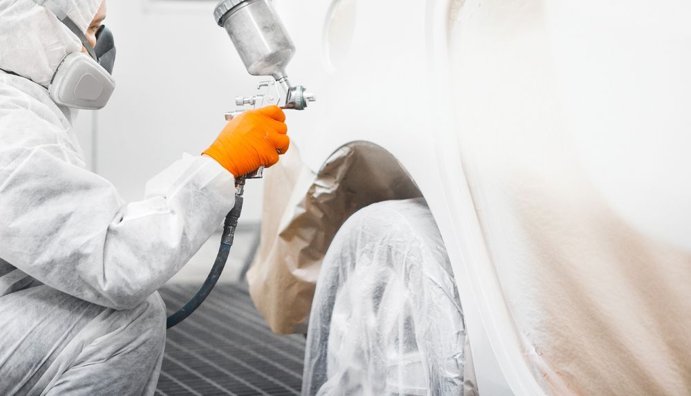 A man in a protective suit is spray painting a car.